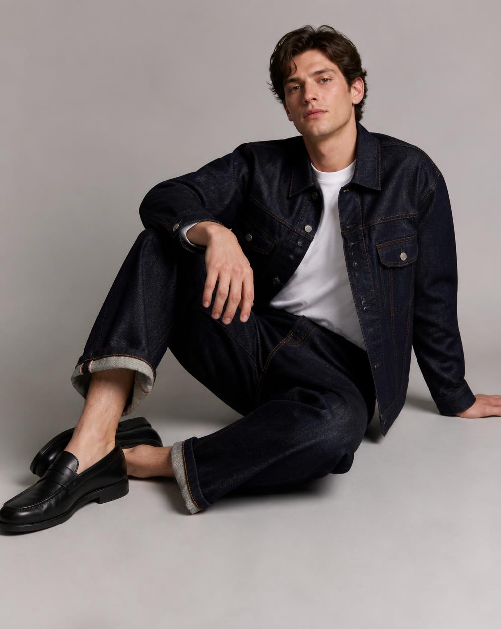 A man seated wearing selvedge denim jeans and a matching denim jacket