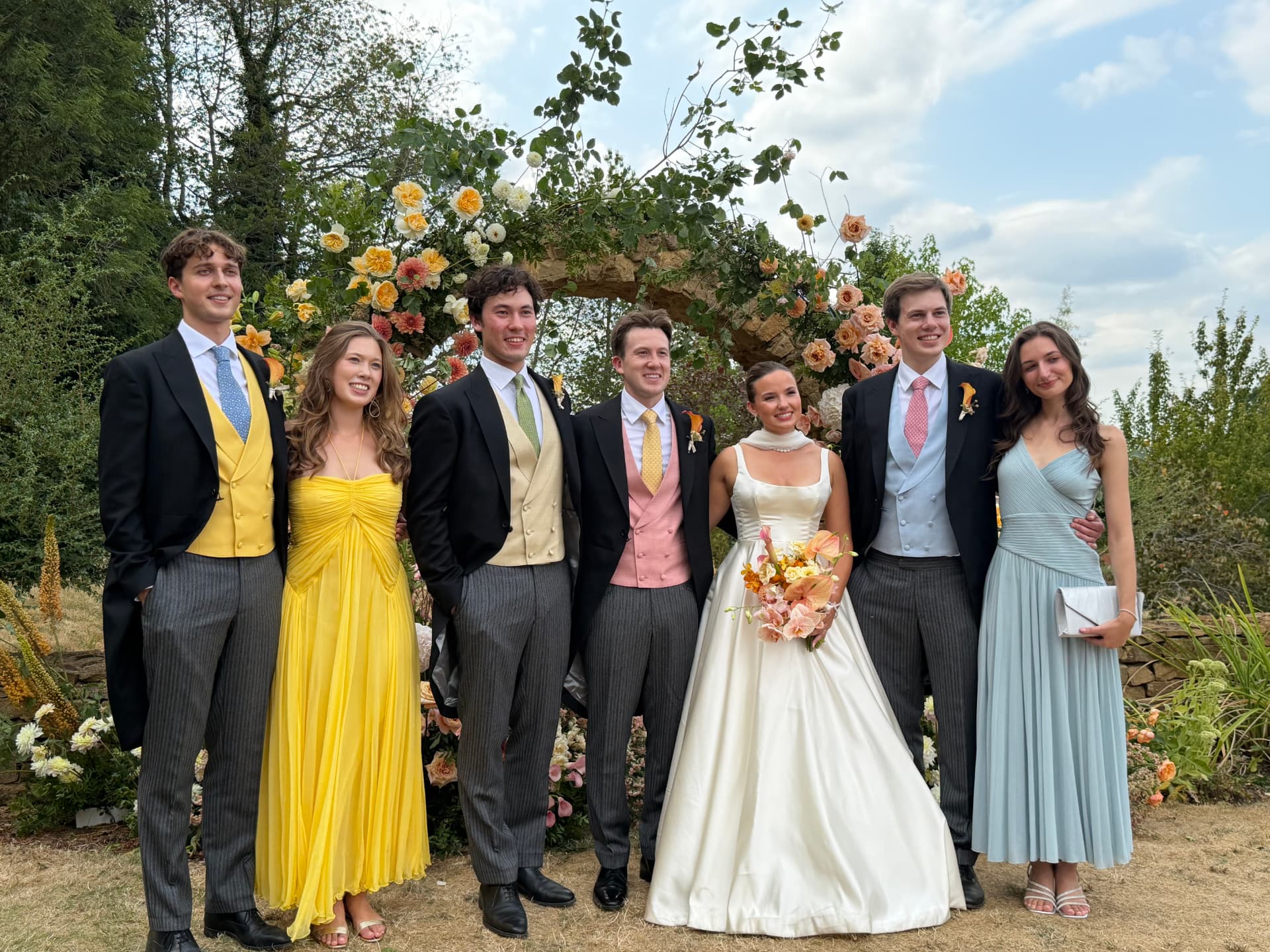 A wedding party in morning dress with colourful waistcoats beside the bride
